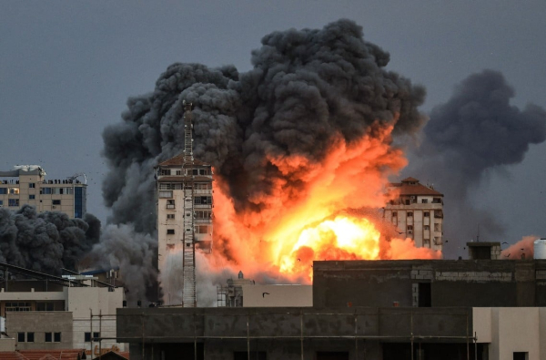 Personas paradas en una terraza observan cómo una bola de fuego y humo se eleva sobre un edificio en la ciudad de Gaza. Foto: MAHMUD HAMS / AFP.