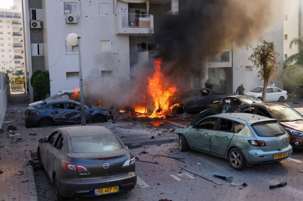 Un miembro de las fuerzas de seguridad israelíes se encuentra cerca de autos en llamas luego de un ataque con cohetes desde la Franja de Gaza en Ashkelon, sur de Israel, el 7 de octubre de 2023. Foto de Ahmad GHARABLI / AFP.