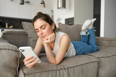 portrait-smiling-young-woman-lying-sofa-home-looking-her-mobile-phone-reading-message.jpg